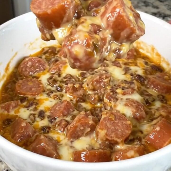 A black slow cooker filled with a creamy, melted chili and cheese dip topped with hot dog slices.