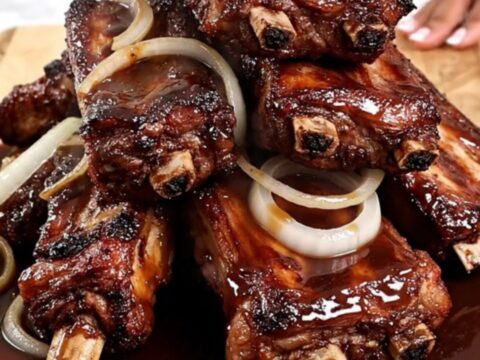 A top-down view of tender slow-cooked spareribs in a black slow cooker with caramelized onions.