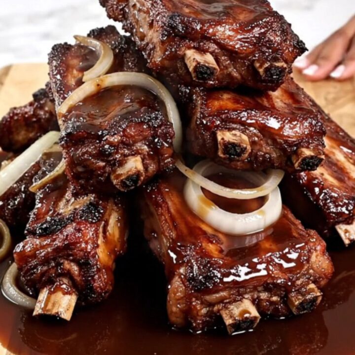 A top-down view of tender slow-cooked spareribs in a black slow cooker with caramelized onions.