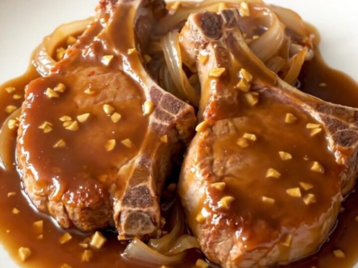 A close-up of tender, braised pork chops in a rich brown sugar and garlic soy sauce in a black slow cooker.