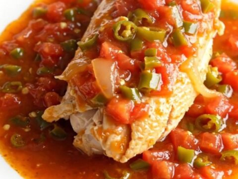 Whole slow-cooked chicken breasts in a creamy stoneware crock with tomato and green chile sauce.