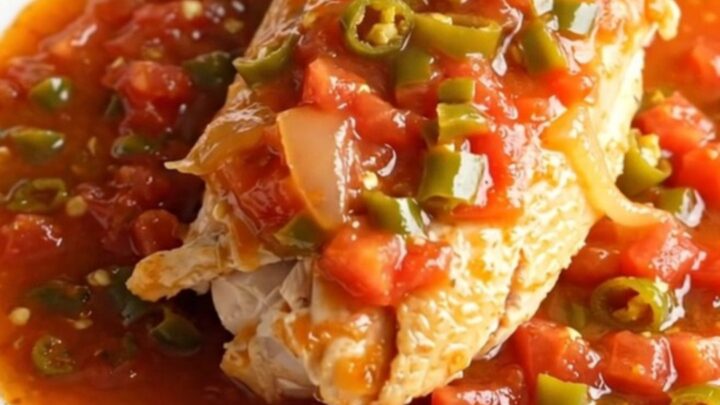 Whole slow-cooked chicken breasts in a creamy stoneware crock with tomato and green chile sauce.