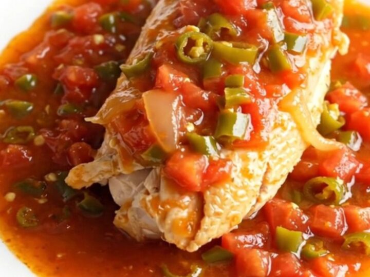 Whole slow-cooked chicken breasts in a creamy stoneware crock with tomato and green chile sauce.