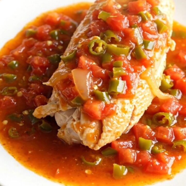 Whole slow-cooked chicken breasts in a creamy stoneware crock with tomato and green chile sauce.