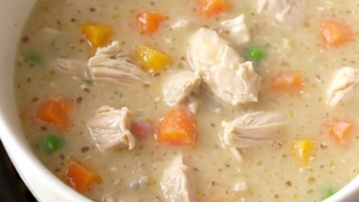 A warm, creamy chicken pot pie soup in a rustic stoneware bowl, garnished with fresh herbs