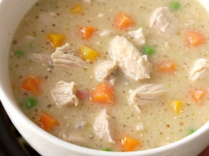 A warm, creamy chicken pot pie soup in a rustic stoneware bowl, garnished with fresh herbs