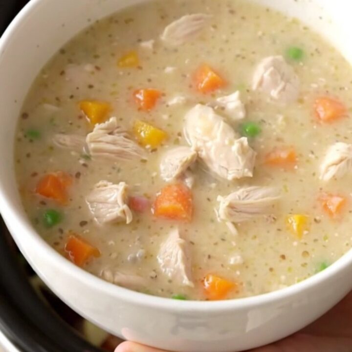 A warm, creamy chicken pot pie soup in a rustic stoneware bowl, garnished with fresh herbs