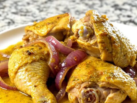 A bowl of tender, yellow-spiced chicken shawarma with soft red onions in a slow cooker.