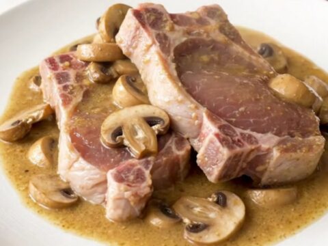 A top-down view of raw boneless pork chops and sliced mushrooms in a slow cooker, ready for cooking.