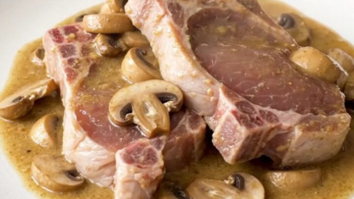 A top-down view of raw boneless pork chops and sliced mushrooms in a slow cooker, ready for cooking.