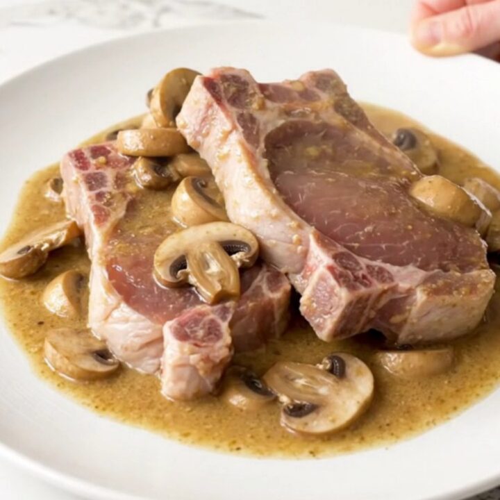 A top-down view of raw boneless pork chops and sliced mushrooms in a slow cooker, ready for cooking.