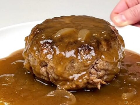 A close-up of tender turkey burger steaks smothered in a rich, glossy brown onion gravy in a black slow cooker.