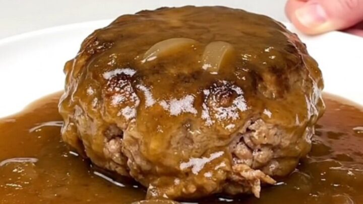 A close-up of tender turkey burger steaks smothered in a rich, glossy brown onion gravy in a black slow cooker.