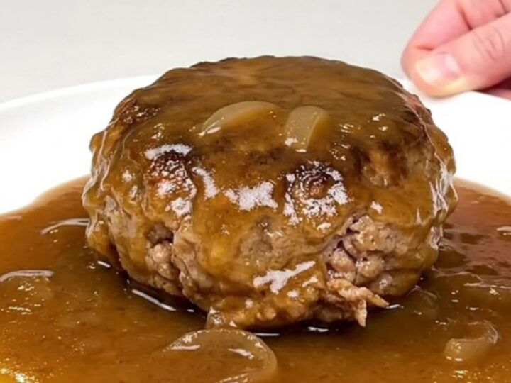 A close-up of tender turkey burger steaks smothered in a rich, glossy brown onion gravy in a black slow cooker.