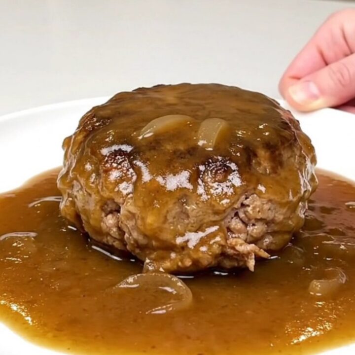 A close-up of tender turkey burger steaks smothered in a rich, glossy brown onion gravy in a black slow cooker.