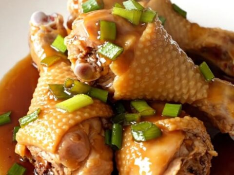 A close-up of honey soy glazed chicken drumsticks in a slow cooker, featuring a rich, dark sauce and sprinkled green onions.