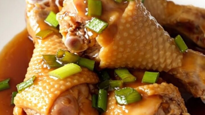A close-up of honey soy glazed chicken drumsticks in a slow cooker, featuring a rich, dark sauce and sprinkled green onions.
