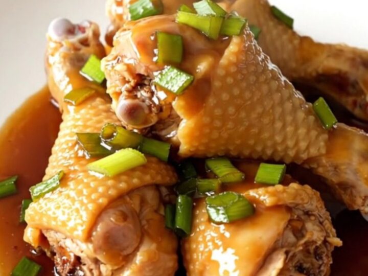 A close-up of honey soy glazed chicken drumsticks in a slow cooker, featuring a rich, dark sauce and sprinkled green onions.