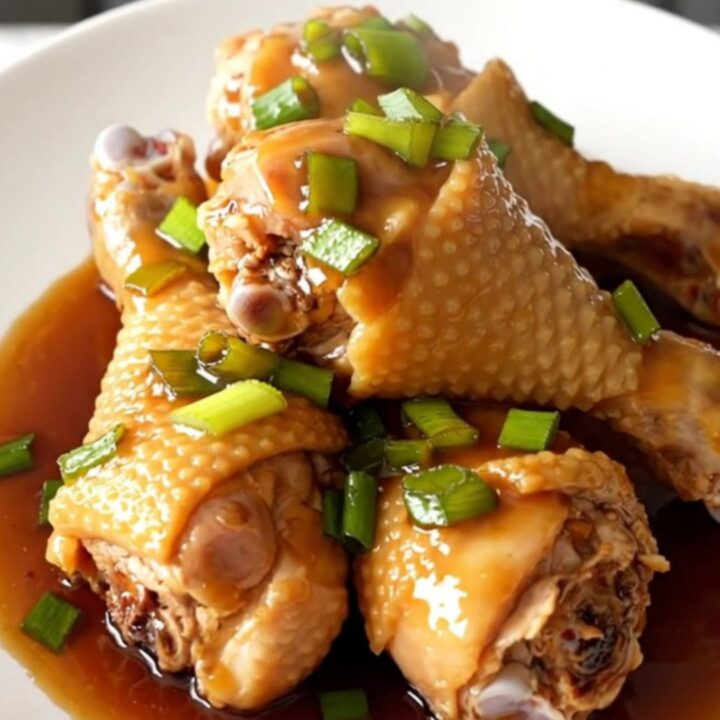 A close-up of honey soy glazed chicken drumsticks in a slow cooker, featuring a rich, dark sauce and sprinkled green onions.