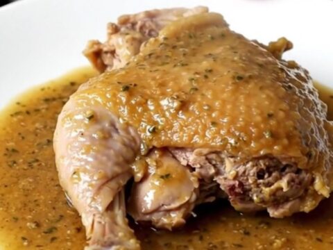 A close-up of a slow cooker filled with braised turkey thighs, carrots, and potatoes in a rich herb gravy.