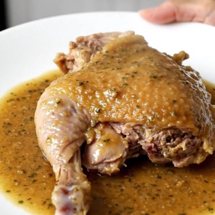 A close-up of a slow cooker filled with braised turkey thighs, carrots, and potatoes in a rich herb gravy.