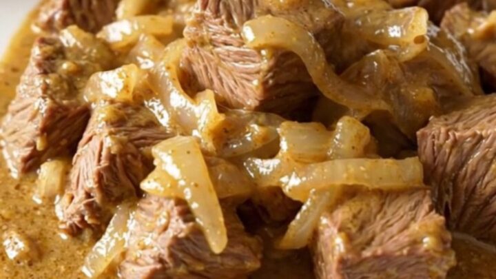 A close-up of tender beef cubes covered in a rich, creamy onion sauce served on a white plate.
