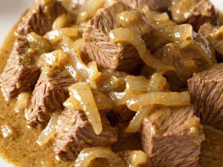 A close-up of tender beef cubes covered in a rich, creamy onion sauce served on a white plate.