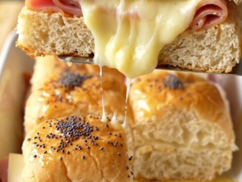 A close-up of baked ham and Swiss sliders with golden brown tops sprinkled with poppy seeds.