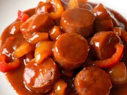 A top-down view of cooked smoked sausage and green peppers coated in a thick, glossy red gochujang sauce.