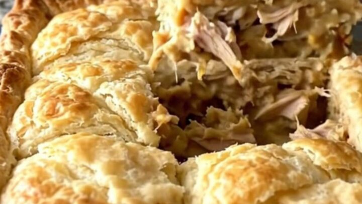 A golden-brown crescent-topped chicken pot pie in a white baker on a speckled countertop.