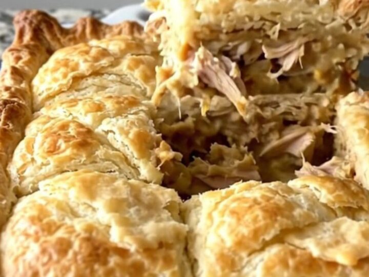 A golden-brown crescent-topped chicken pot pie in a white baker on a speckled countertop.