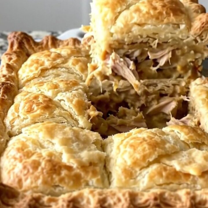 A golden-brown crescent-topped chicken pot pie in a white baker on a speckled countertop.
