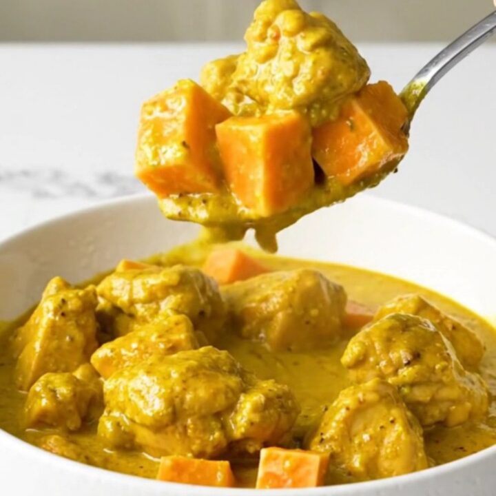 A top-down view of a black slow cooker filled with chicken and sweet potatoes in a golden coconut curry sauce.