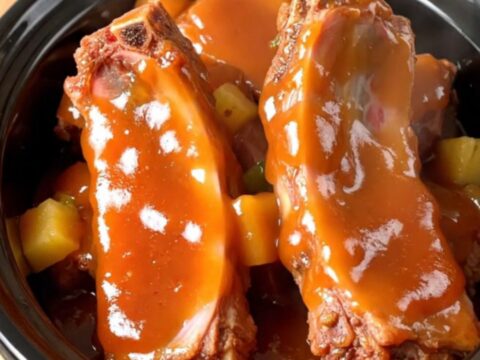 Slow cooker filled with tender spareribs, pineapple chunks, and green peppers in a glossy sweet and sour sauce.