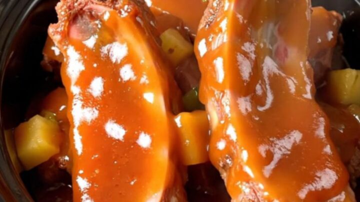 Slow cooker filled with tender spareribs, pineapple chunks, and green peppers in a glossy sweet and sour sauce.