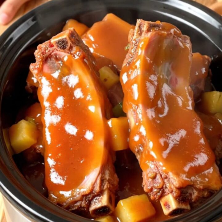 Slow cooker filled with tender spareribs, pineapple chunks, and green peppers in a glossy sweet and sour sauce.