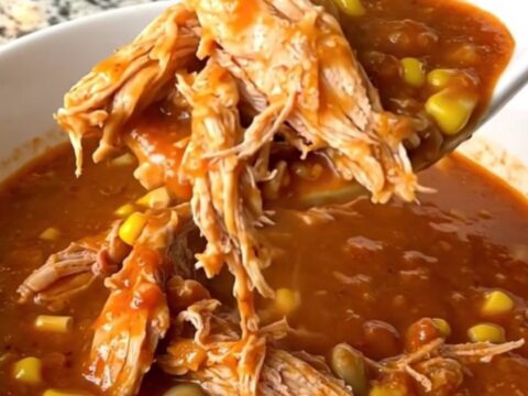 A rustic bowl of smoky Brunswick stew filled with shredded chicken, corn, and lima beans in a thick red sauce.