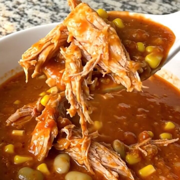 A rustic bowl of smoky Brunswick stew filled with shredded chicken, corn, and lima beans in a thick red sauce.