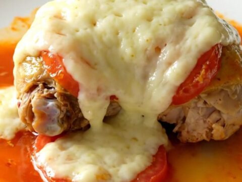 A close-up of tender, braised chicken thighs topped with melted mozzarella and cooked Roma tomatoes in a slow cooker.
