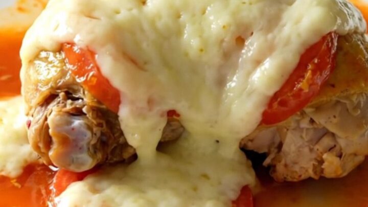 A close-up of tender, braised chicken thighs topped with melted mozzarella and cooked Roma tomatoes in a slow cooker.