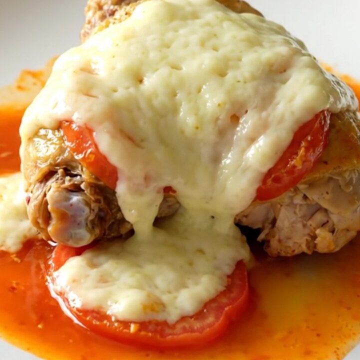 A close-up of tender, braised chicken thighs topped with melted mozzarella and cooked Roma tomatoes in a slow cooker.