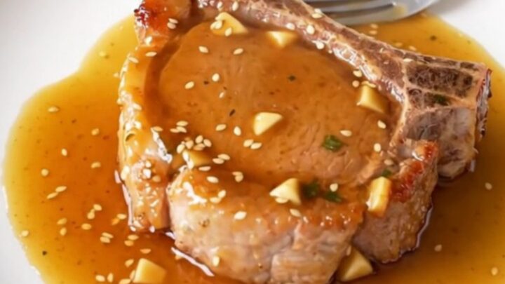 A close-up of slow-cooked bone-in pork chops glazed in a shiny honey garlic sauce served on a plate.