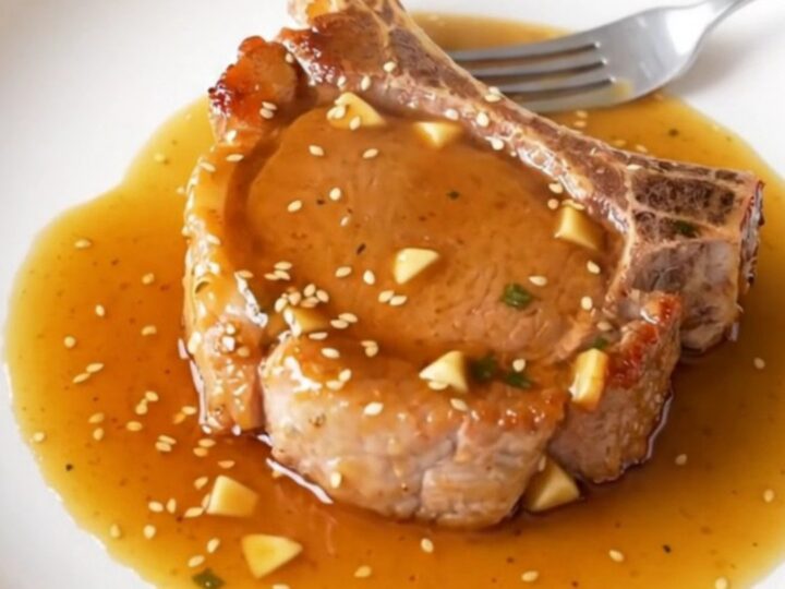 A close-up of slow-cooked bone-in pork chops glazed in a shiny honey garlic sauce served on a plate.