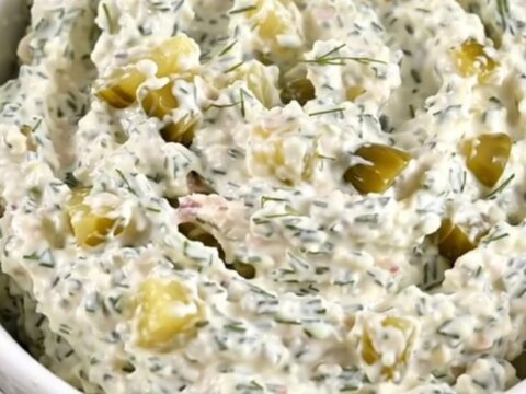 A creamy chicken and dill pickle dip in a white bowl, showing flecks of herbs.