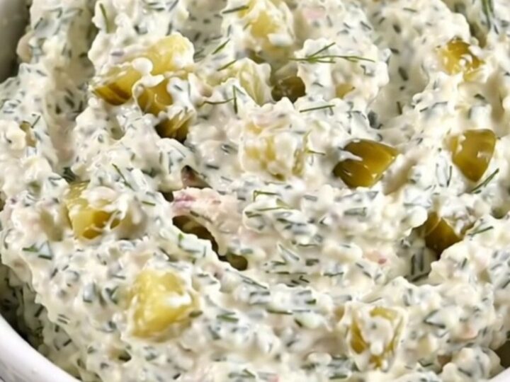 A creamy chicken and dill pickle dip in a white bowl, showing flecks of herbs.