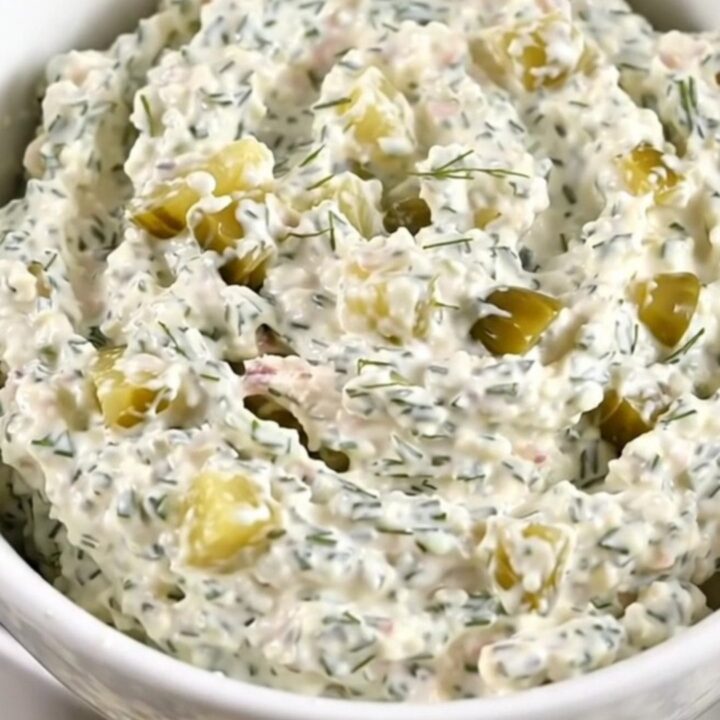 A creamy chicken and dill pickle dip in a white bowl, showing flecks of herbs.