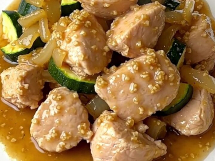 A close-up of tender chicken pieces, zucchini, and onions in a rich garlic butter sauce inside a slow cooker.