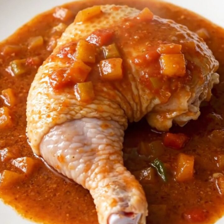 A close-up of a slow cooker filled with chicken leg quarters, diced vegetables, and a rich red tomato-based Creole sauce.