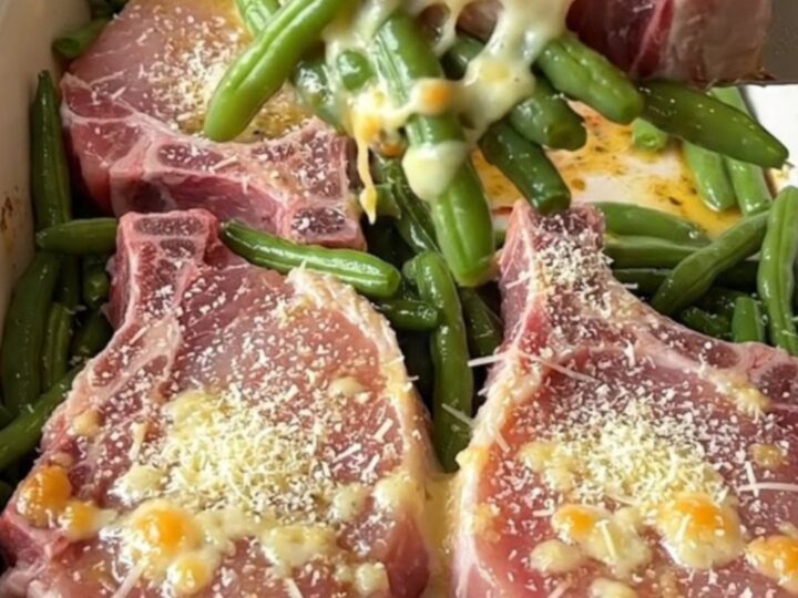 A top-down view of a rectangular baking dish filled with raw pork chops and fresh green beans, ready for the oven.