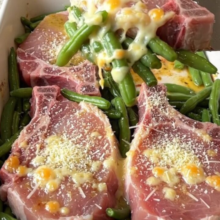 A top-down view of a rectangular baking dish filled with raw pork chops and fresh green beans, ready for the oven.